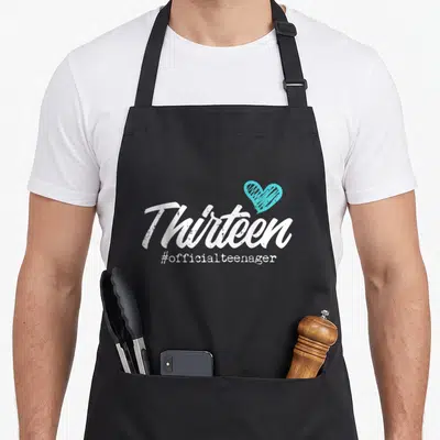 Thirteen 13th birthday apron - White Thirteen script with teal heart and #officialteenager text below — shown on a black cotton canvas apron against a white background