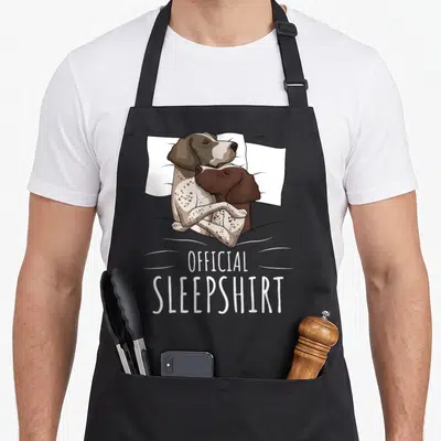 Pointer gsp dog apron - Two cartoon dogs cuddling on a pillow with official sleepshirt text below — shown on a black cotton canvas apron against a white background