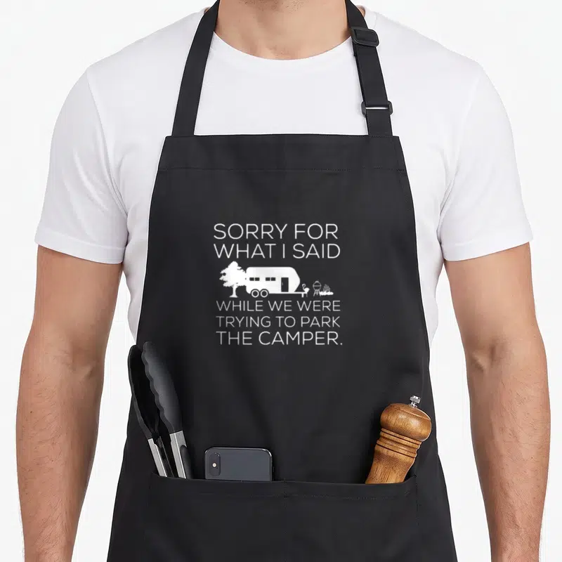 Sorry rv apron - White text sorry for what i said with camper and camping icons on grey background — shown on a black cotton canvas apron against a white background