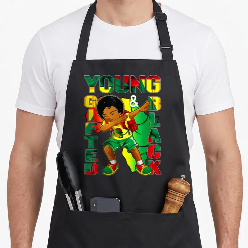 History gifted apron - Cartoon boy dabbing surrounded by YOUNG GIFTED & BLACK text in red green and yellow patterns — shown on a black cotton canvas apron against a white background