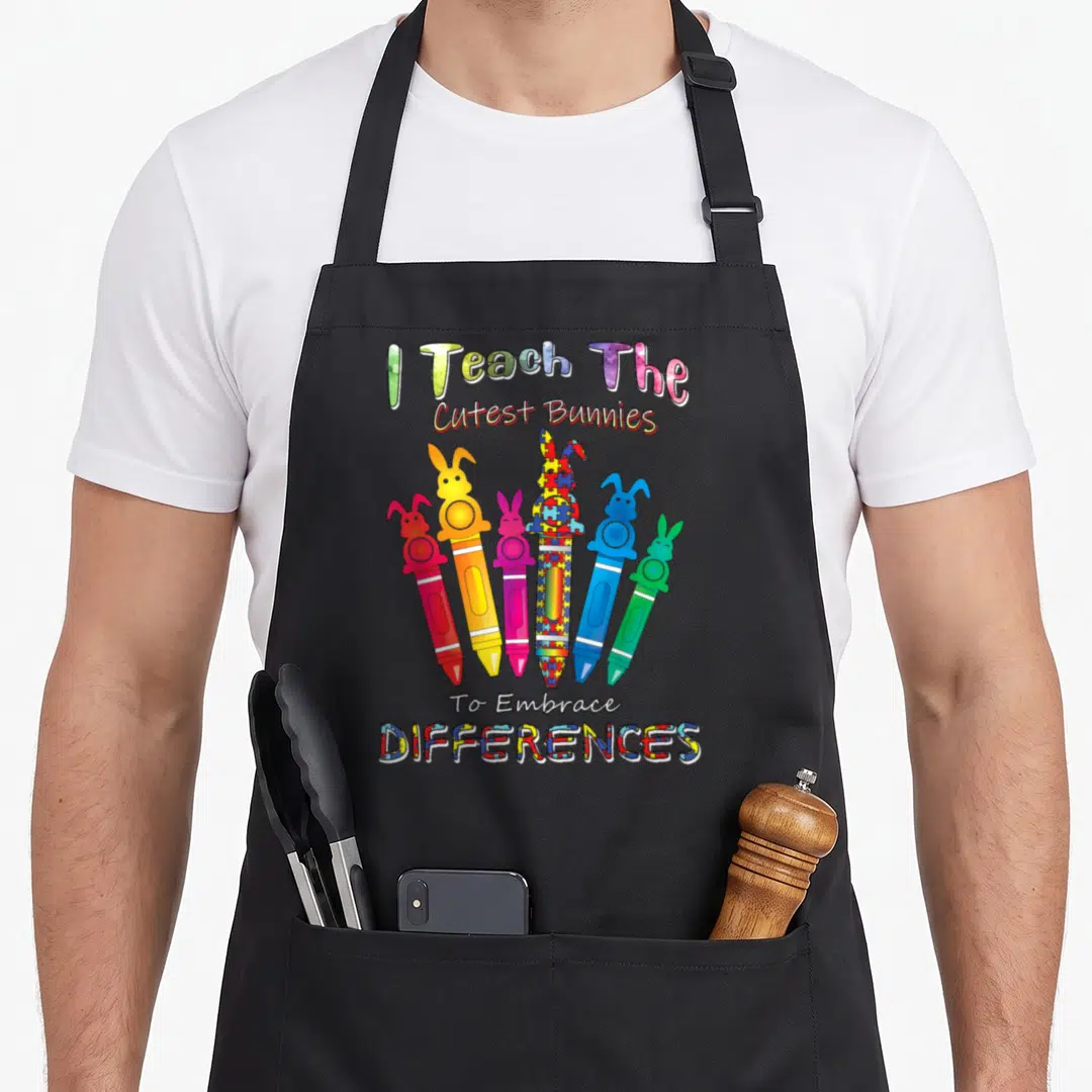 Autism teacher apron - Six bunny crayons in red orange pink blue green yellow with puzzle pieces and text I Teach — shown on a black cotton canvas apron against a white background