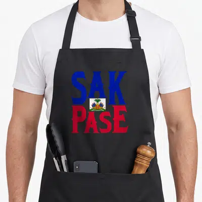 Pase haitian pride apron - Blue SAK and red PASE text with Haitian coat of arms centered between them — shown on a black cotton canvas apron against a white background