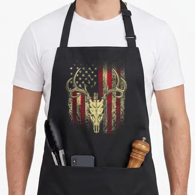 Antler american flag apron - Tan deer skull with antlers over distressed red stripes and tan stars — shown on a black cotton canvas apron against a white background