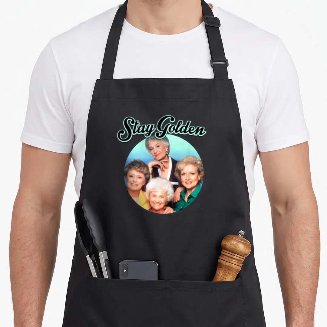 Science golden apron - Stay Golden text above circular photo of four smiling women in blue and green — shown on a black cotton canvas apron against a white background