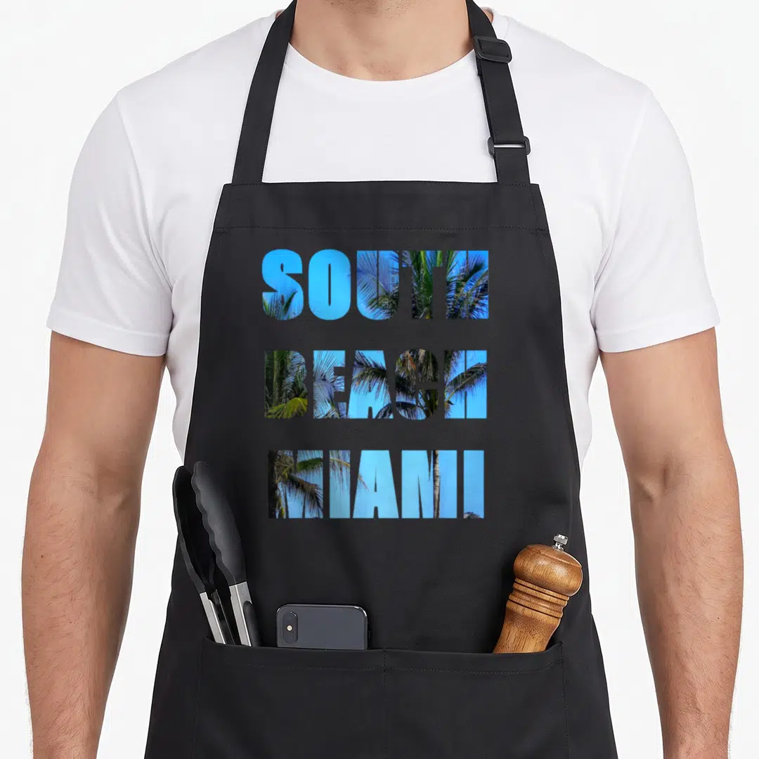 South miami beach apron - Stacked text SOUTH BEACH MIAMI filled with palm tree photo and blue sky — shown on a black cotton canvas apron against a white background