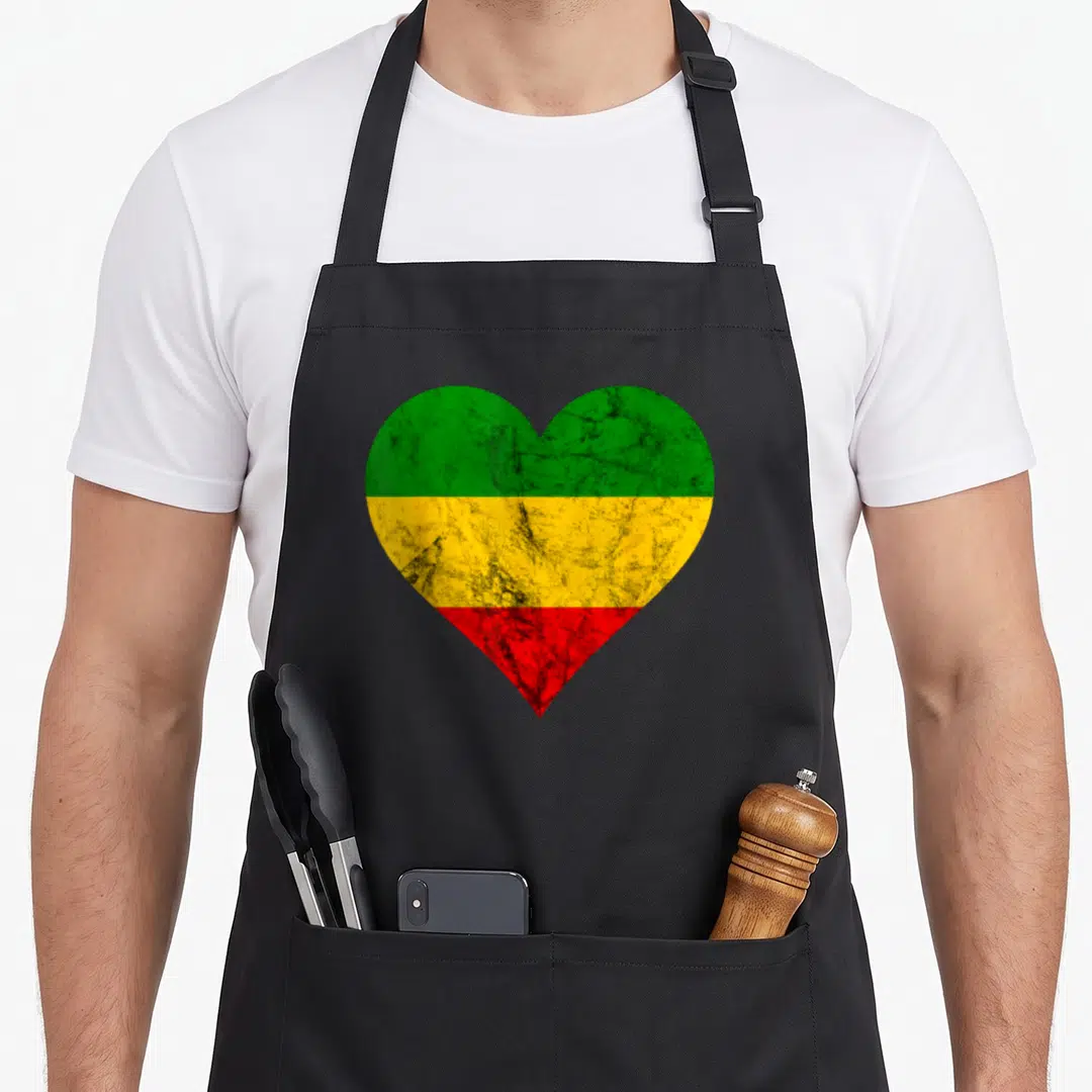 Rastafarian reggaeton apron - Distressed heart shape with three horizontal stripes in green, yellow, and red — shown on a black cotton canvas apron against a white background