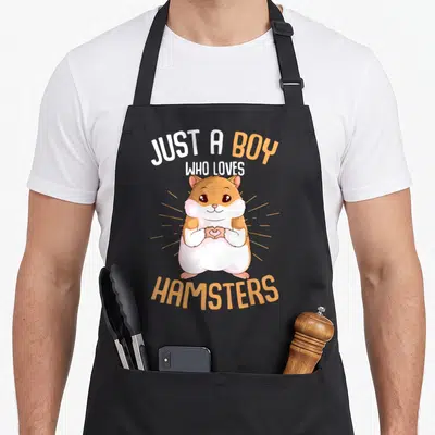 Hammy hamster mom apron - Cartoon hamster making heart with paws and text Just A Boy Who Loves Hamsters — shown on a black cotton canvas apron against a white background