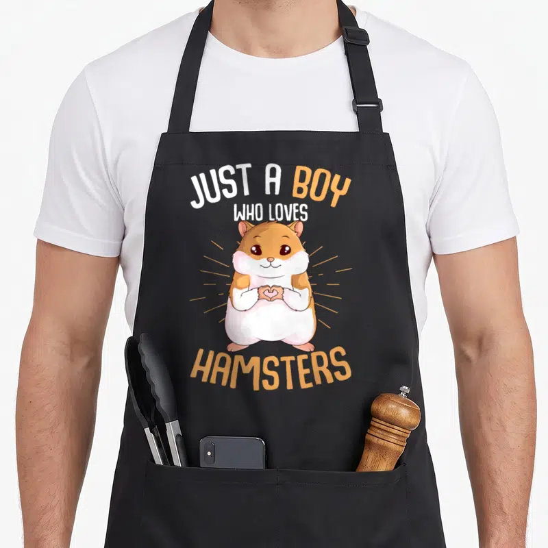 Hammy hamster mom apron - Cartoon hamster making heart with paws and text Just A Boy Who Loves Hamsters — shown on a black cotton canvas apron against a white background