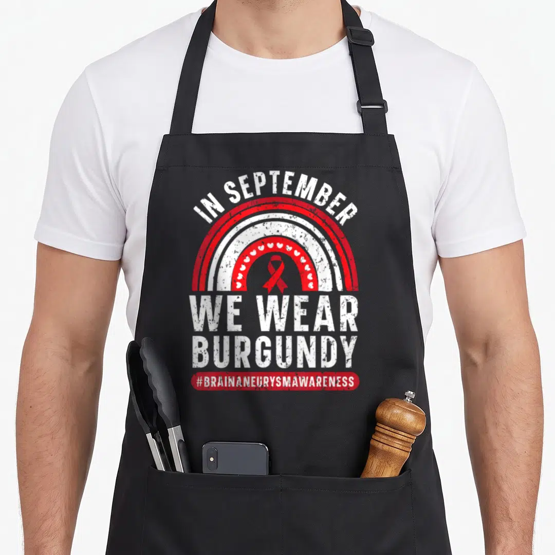 September aneurysm awareness apron - Distressed burgundy and white rainbow with hearts and brain aneurysm ribbon text — shown on a black cotton canvas apron against a white background