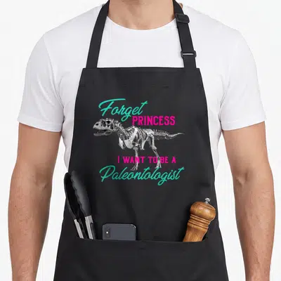 Paleontologist princess apron - Dinosaur skeleton with Forget Princess I Want To Be A Paleontologist text in turquoise — shown on a black cotton canvas apron against a white background