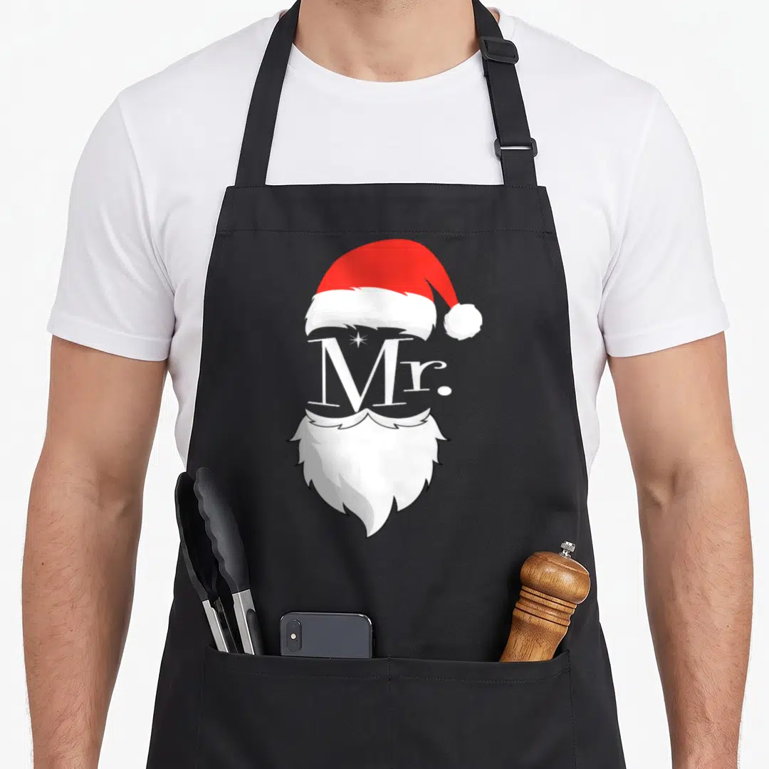 Claus mr mrs aprons - Red Santa hat, white Mr text, and white beard stacked vertically on black background — shown on a black cotton canvas apron against a white background