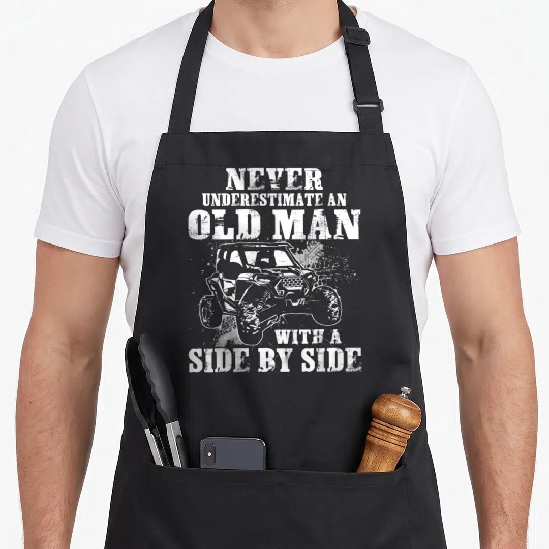 Underestimate utv apron - Distressed white text surrounding a grey side-by-side vehicle graphic with dirt splatter — shown on a black cotton canvas apron against a white background