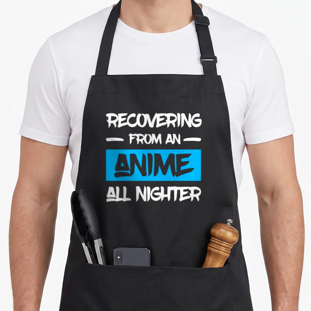 Recovering anime apron - Stacked white and grey text reading Recovering from an anime all nighter on blue rectangle — shown on a black cotton canvas apron against a white background