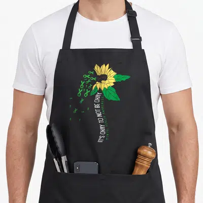 Awareness sunflower apron - Yellow sunflower with green ribbons and vertical white text IT'S OKAY TO NOT BE OKAY — shown on a black cotton canvas apron against a white background