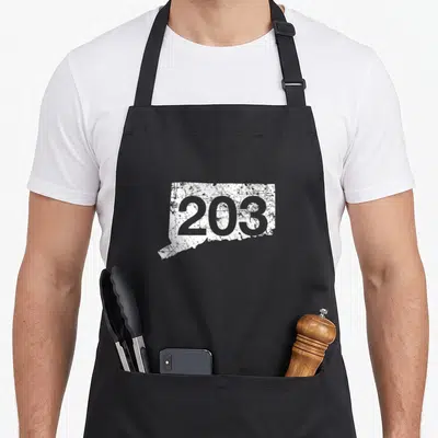 Stamford nutmeg apron - Distressed white Connecticut map silhouette with grey 203 area code text — shown on a black cotton canvas apron against a white background
