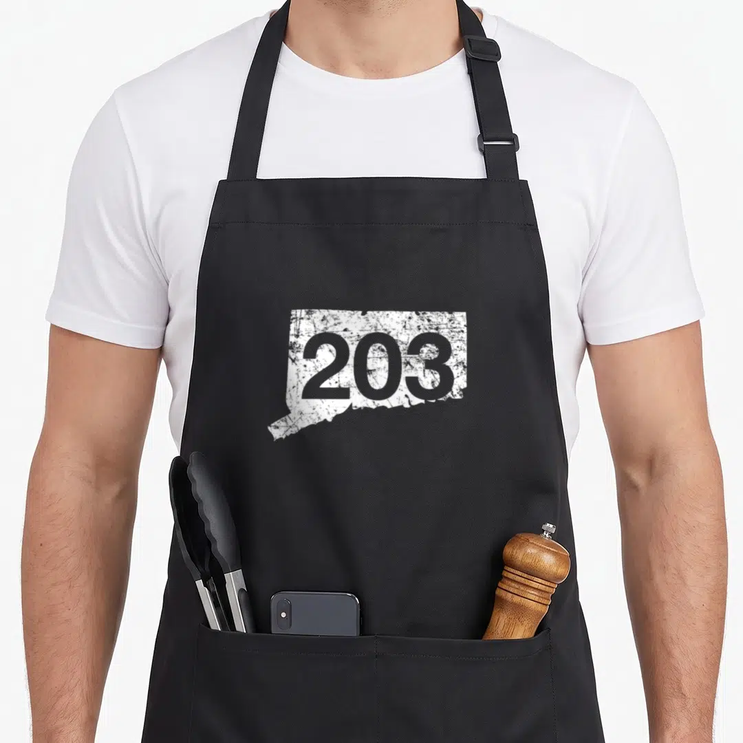 Stamford nutmeg apron - Distressed white Connecticut map silhouette with grey 203 area code text — shown on a black cotton canvas apron against a white background