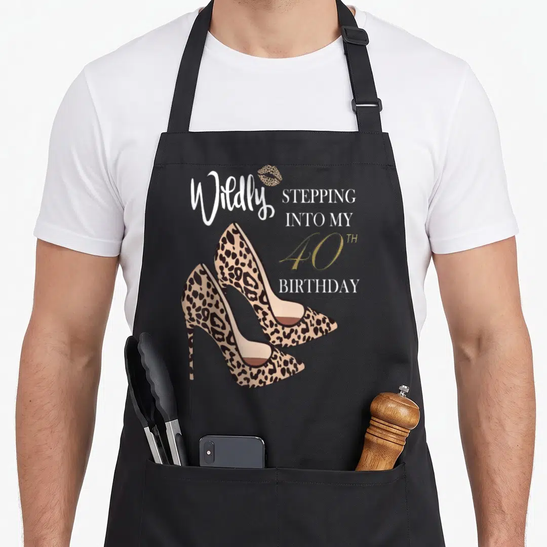 Stepping 40th birthday apron - Leopard print high heels and Wildly Stepping Into My 40th Birthday text in white and gold — shown on a black cotton canvas apron against a white background
