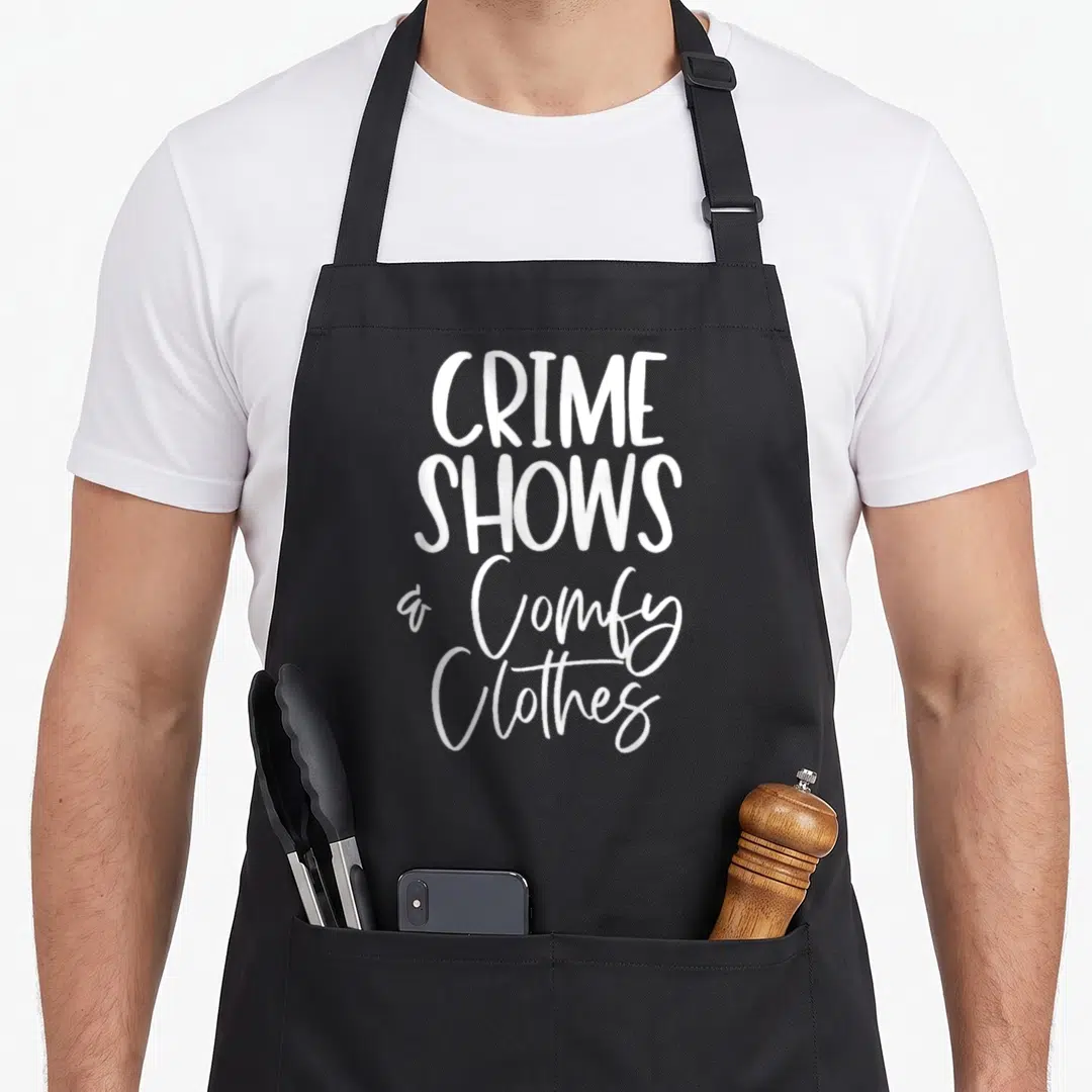 Crime mystery apron - White stacked typography reading CRIME SHOWS & Comfy Clothes — shown on a black cotton canvas apron against a white background