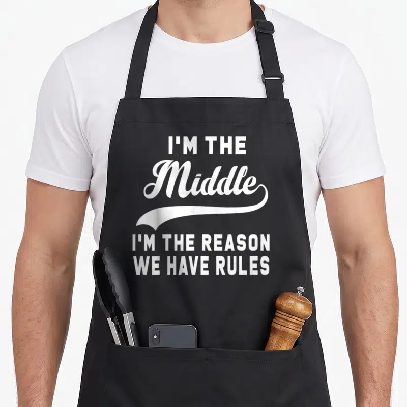 Reason oldest child apron - White typography text I'm the Middle I'm the Reason We Have Rules with swoosh on black — shown on a black cotton canvas apron against a white background