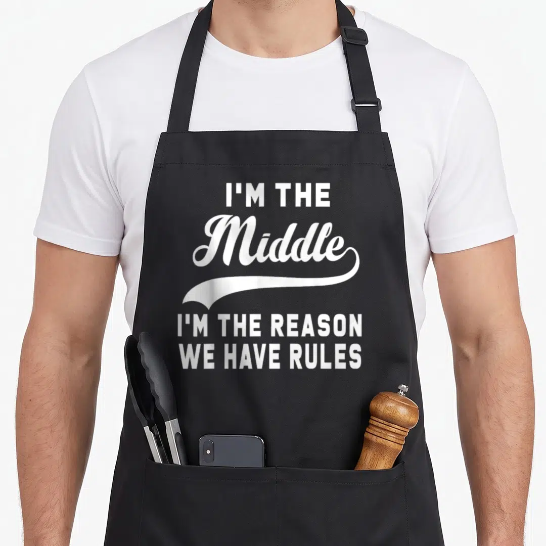 Reason oldest child apron - White typography text I'm the Middle I'm the Reason We Have Rules with swoosh on black — shown on a black cotton canvas apron against a white background