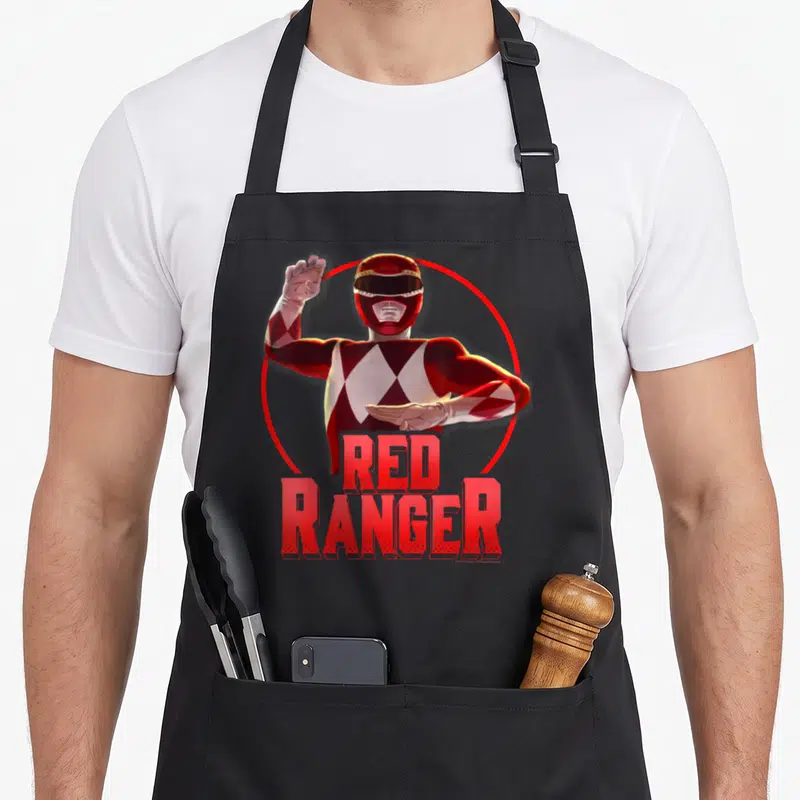 Action rangers apron - Realistic Red Ranger in karate pose inside red circle with bold red text — shown on a black cotton canvas apron against a white background