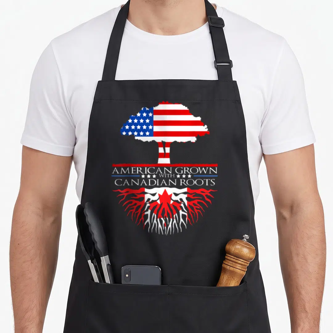 Canadian root american flag apron - Tree with US flag canopy and Canadian maple leaf roots surrounding text AMERICAN — shown on a black cotton canvas apron against a white background