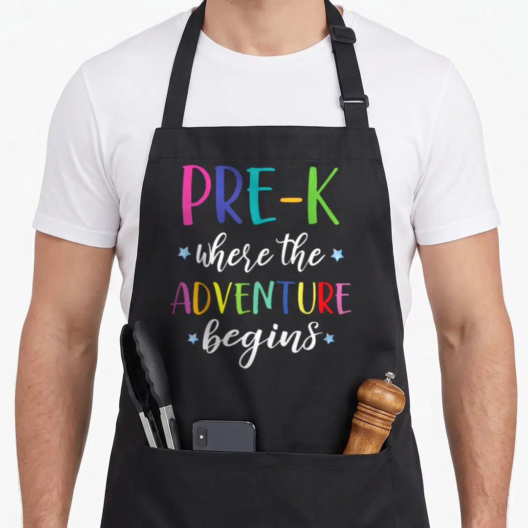 Teacher preschool apron - Stacked PRE-K text with small blue stars in pink, blue, green, yellow, and white — shown on a black cotton canvas apron against a white background