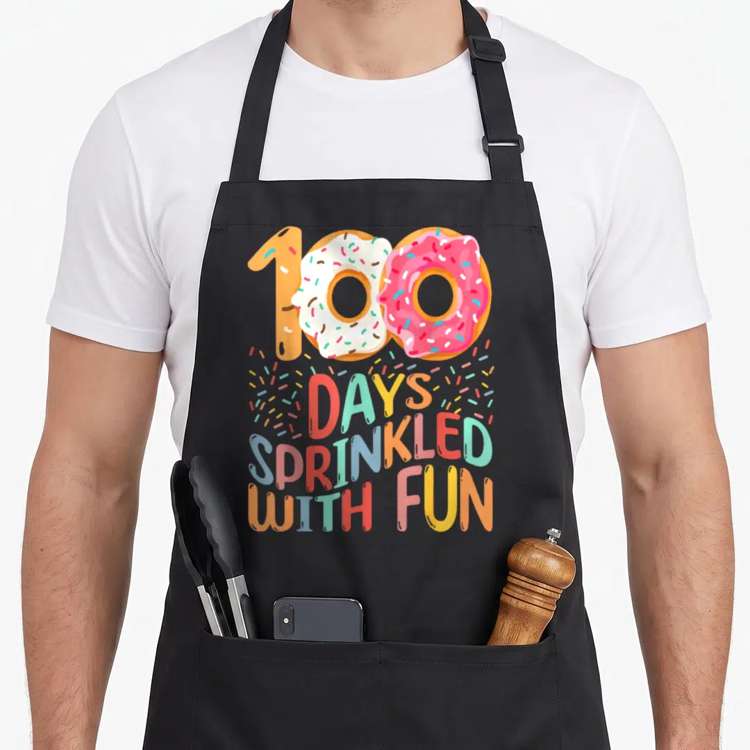 School mentor apron - Two donuts forming 100 with text days sprinkled with fun — shown on a black cotton canvas apron against a white background