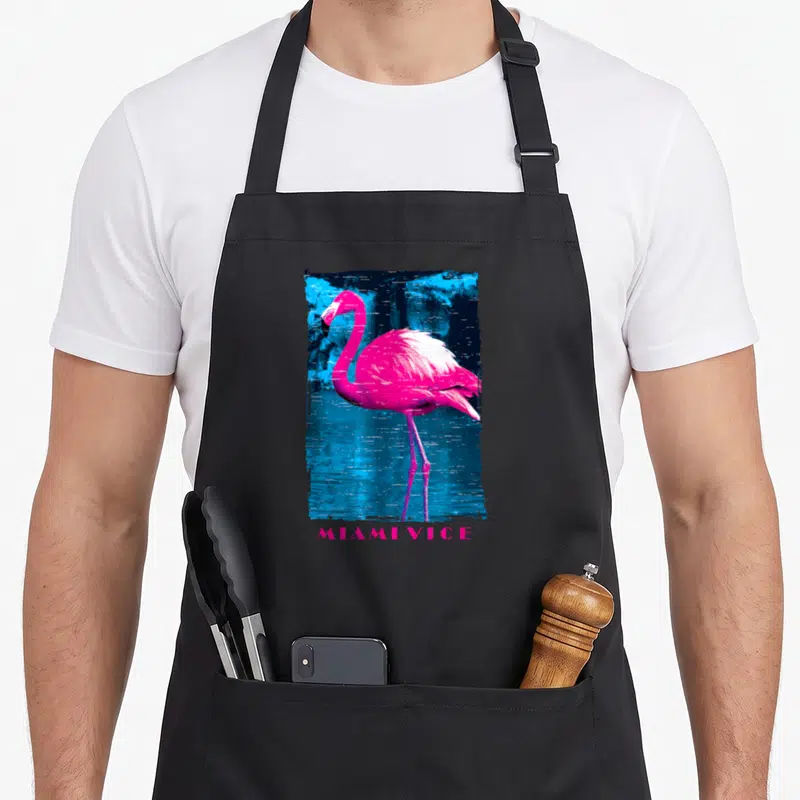 Miami pink flamingo apron - Pink flamingo inside distressed blue black rectangle with MIAMI VICE text below — shown on a black cotton canvas apron against a white background