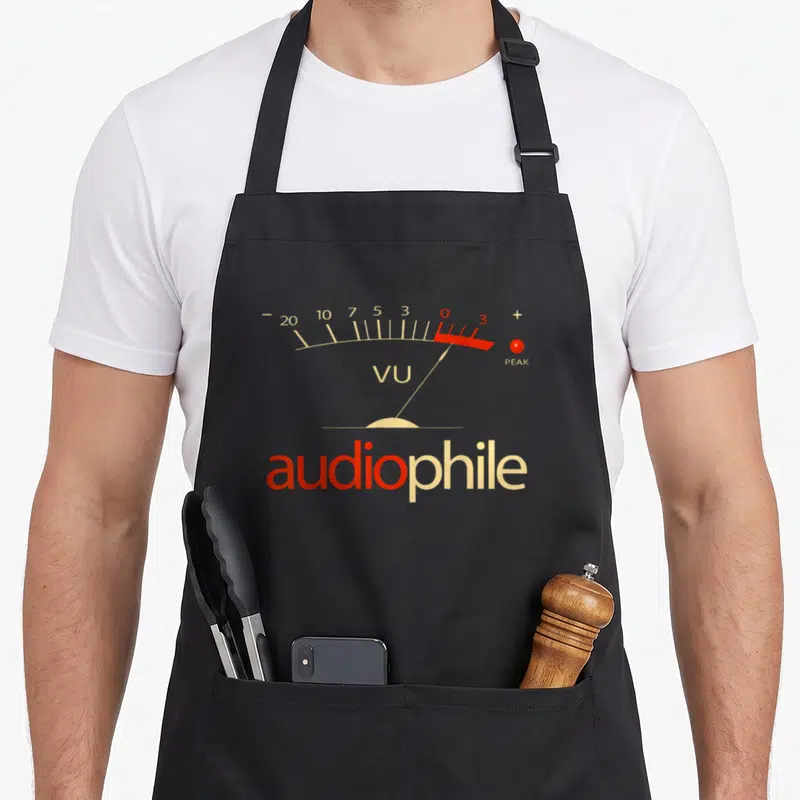 Meter audiophile apron - VU meter scale with beige numbers, red needle, and audiophile text — shown on a black cotton canvas apron against a white background