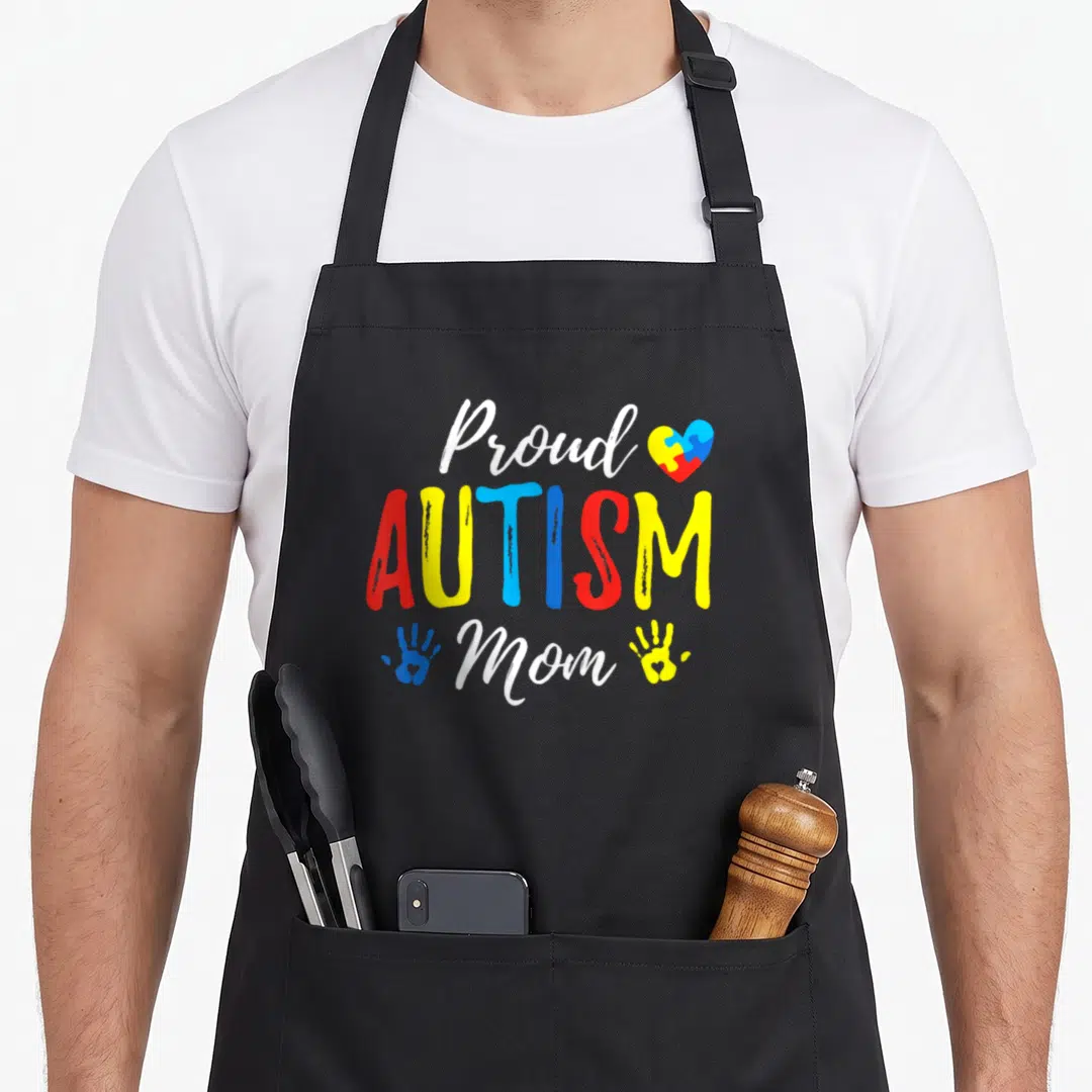 Proud family aprons - Proud AUTISM Mom text with puzzle heart and colored handprints — shown on a black cotton canvas apron against a white background