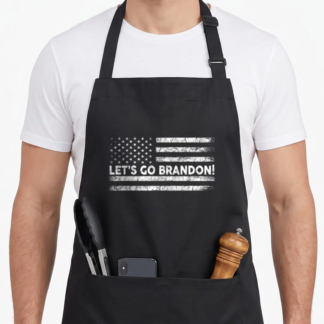 Brandon flag apron - Distressed white USA flag with LET'S GO BRANDON! text across center — shown on a black cotton canvas apron against a white background