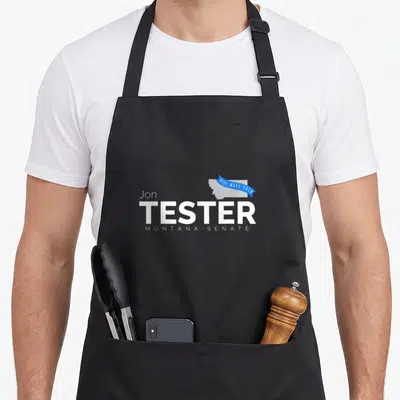 Jon midterms apron - Jon Tester Montana Senate 2018 Blue Wave logo with grey Montana map and blue ribbon — shown on a black cotton canvas apron against a white background