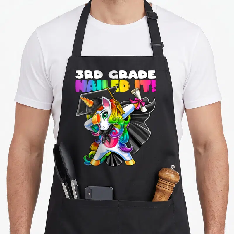 Gown unicorn apron - Dabbing unicorn in cap gown holding diploma with 3rd Grade Nailed It text — shown on a black cotton canvas apron against a white background