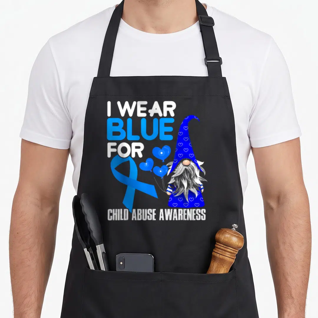 April ribbon apron - Cartoon gnome with blue heart hat holding balloons beside blue ribbon and text I Wear Blue — shown on a black cotton canvas apron against a white background