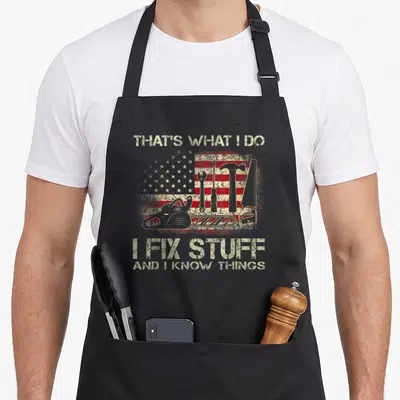 Flag handyman apron - Distressed USA flag with wrench hammer saw and chainsaw overlay and fix stuff text — shown on a black cotton canvas apron against a white background