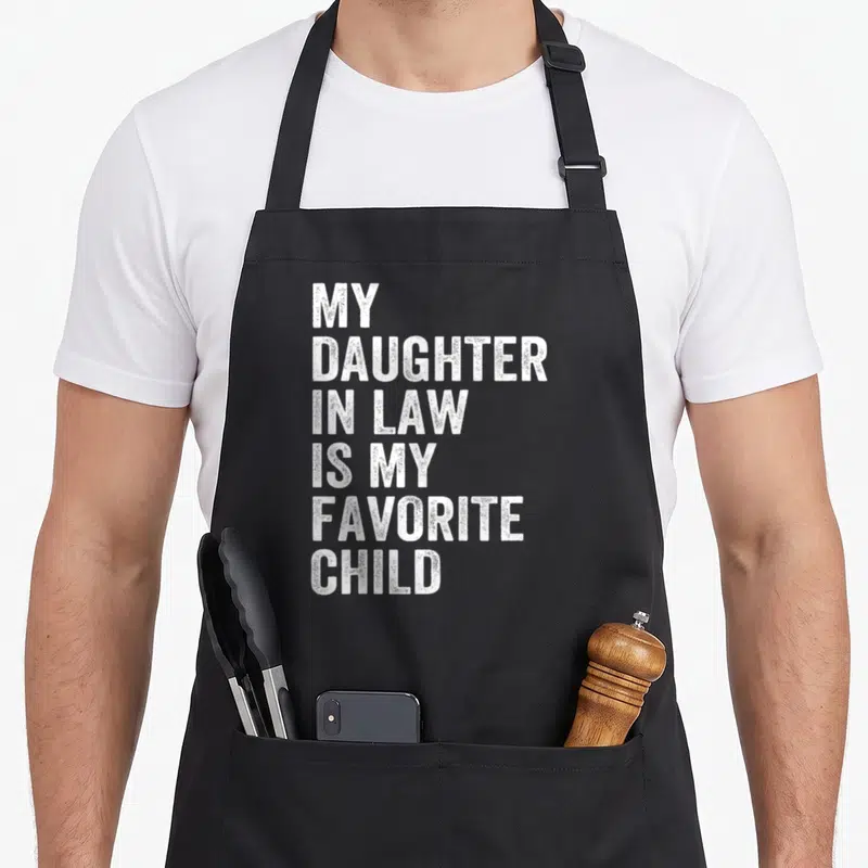 Funny father mom and daughter aprons - White stacked text reading My Daughter In Law Is My Favorite Child on black — shown on a black cotton canvas apron against a white background