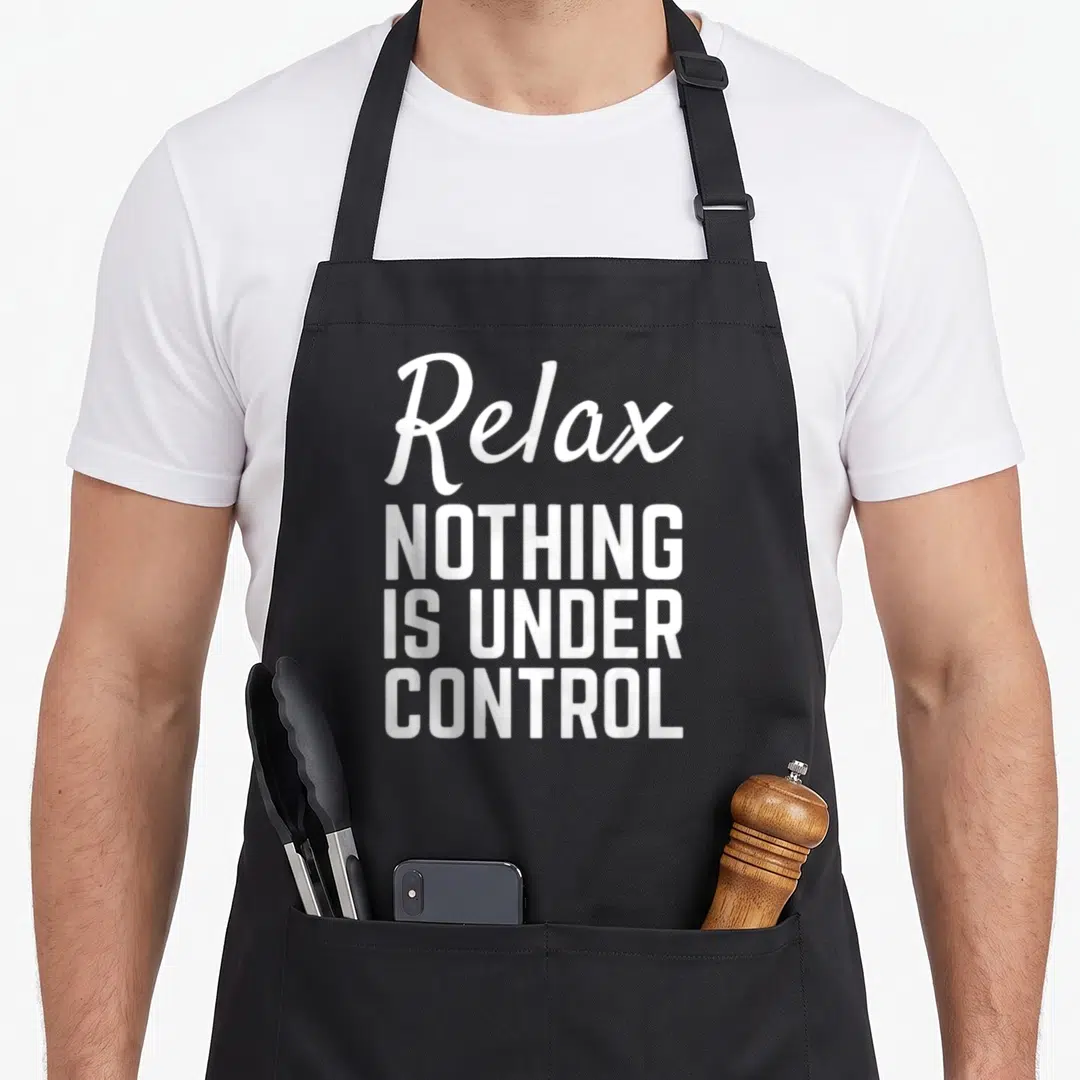 Relax meditation apron - White stacked text reading Relax NOTHING IS UNDER CONTROL on a dark background — shown on a black cotton canvas apron against a white background