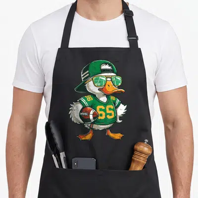 Duck football apron - Cartoon duck in green jersey 65 with sunglasses and football — shown on a black cotton canvas apron against a white background