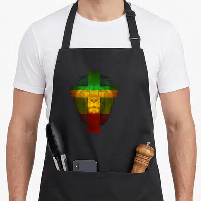Ethiopian cross apron - Realistic lion head overlaid with distressed cross in green yellow red and black — shown on a black cotton canvas apron against a white background