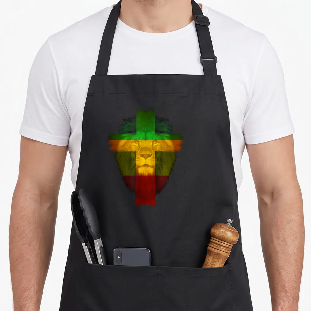 Ethiopian cross apron - Realistic lion head overlaid with distressed cross in green yellow red and black — shown on a black cotton canvas apron against a white background