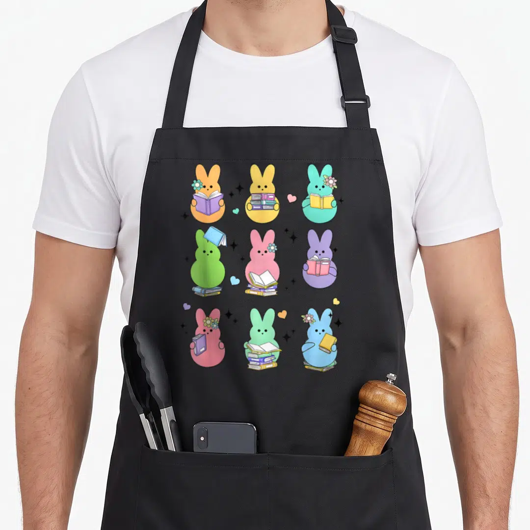 Book easter bunny aprons - Nine cartoon bunnies in pastel colors holding books and stacks in a grid with stars — shown on a black cotton canvas apron against a white background