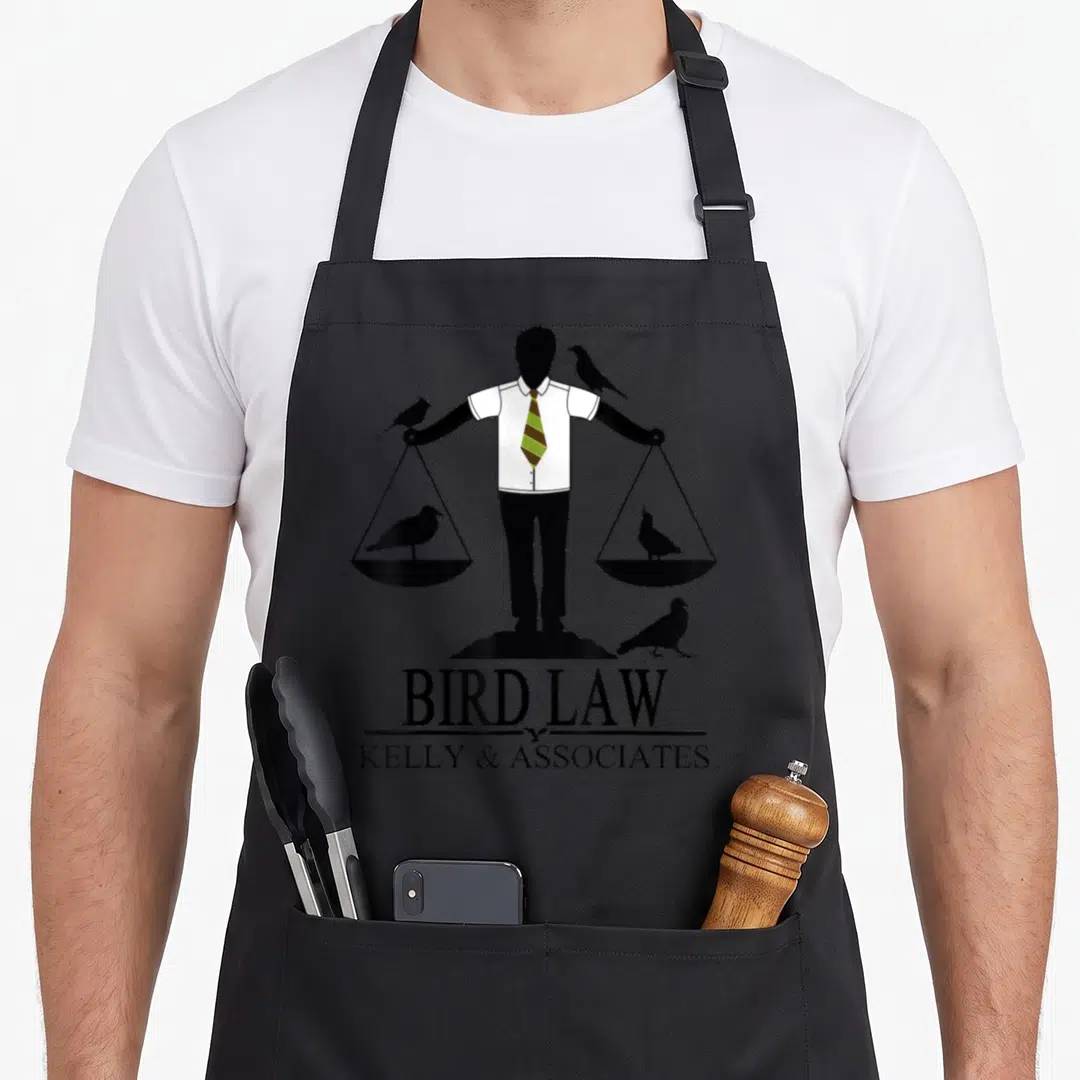 Law meme apron - Lawyer silhouette holding bird scales with BIRD LAW KELLY & ASSOCIATES text — shown on a black cotton canvas apron against a white background