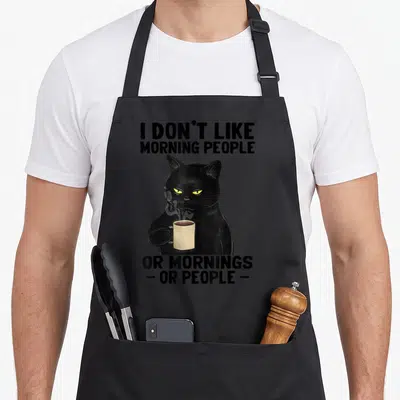 Morning apron or apron - Black cartoon cat holding beige mug with text I don't like morning people — shown on a black cotton canvas apron against a white background