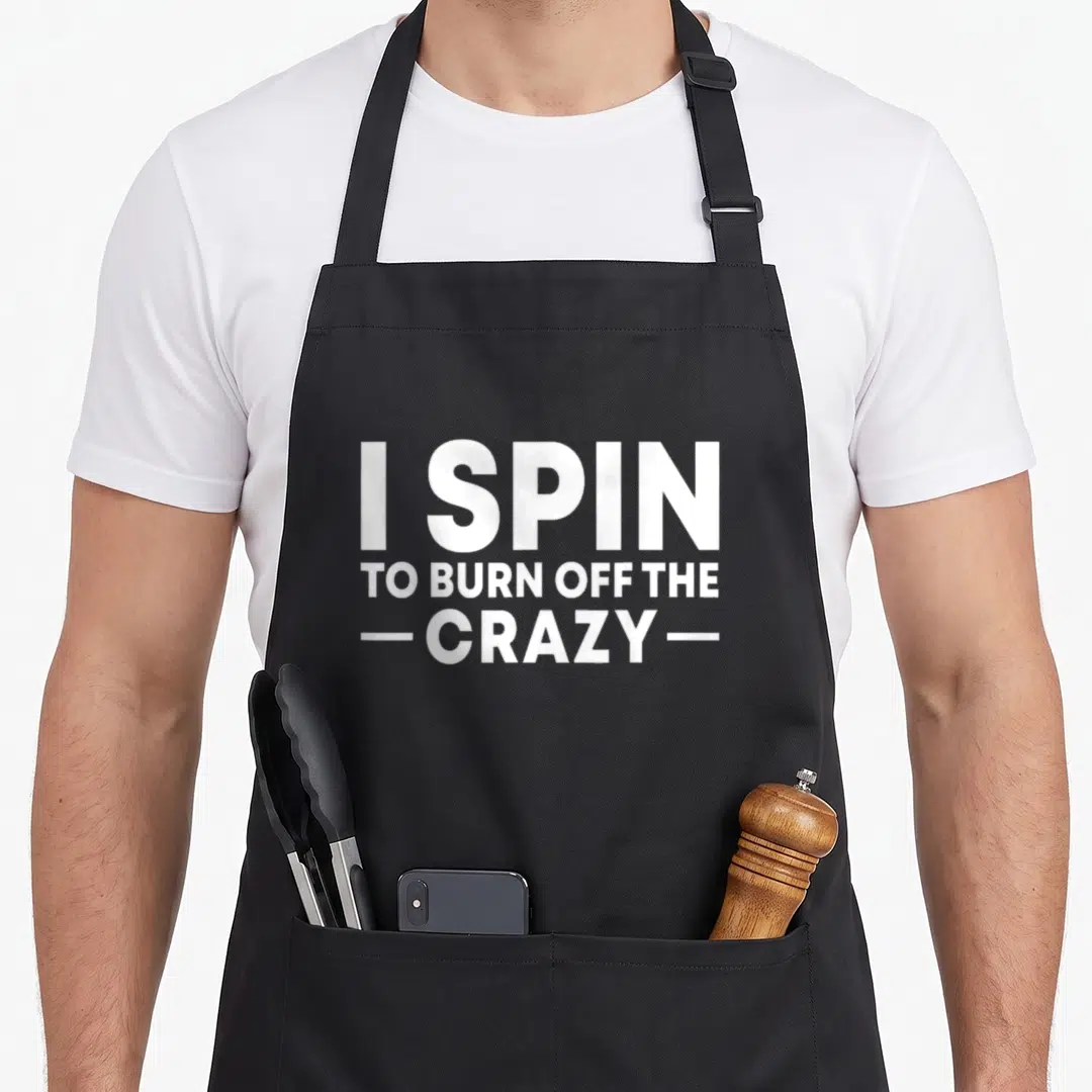 Spin bike apron - White stacked text reading I SPIN TO BURN OFF THE CRAZY on grey background — shown on a black cotton canvas apron against a white background