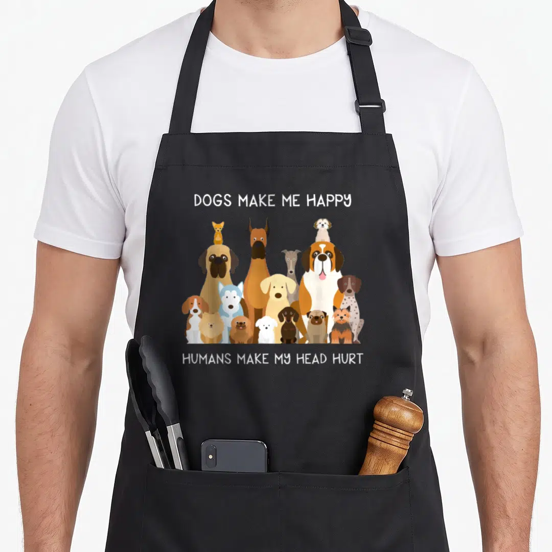 Vintage human dog apron - Cartoon dogs standing together under DOGS MAKE ME HAPPY HUMANS MAKE MY HEAD HURT text — shown on a black cotton canvas apron against a white background