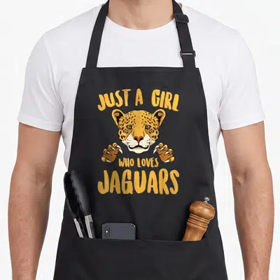 Cute animal apron for grilling - Cartoon jaguar head and paws between yellow text reading Just A Girl Who Loves Jaguars — shown on a black cotton canvas apron against a white background