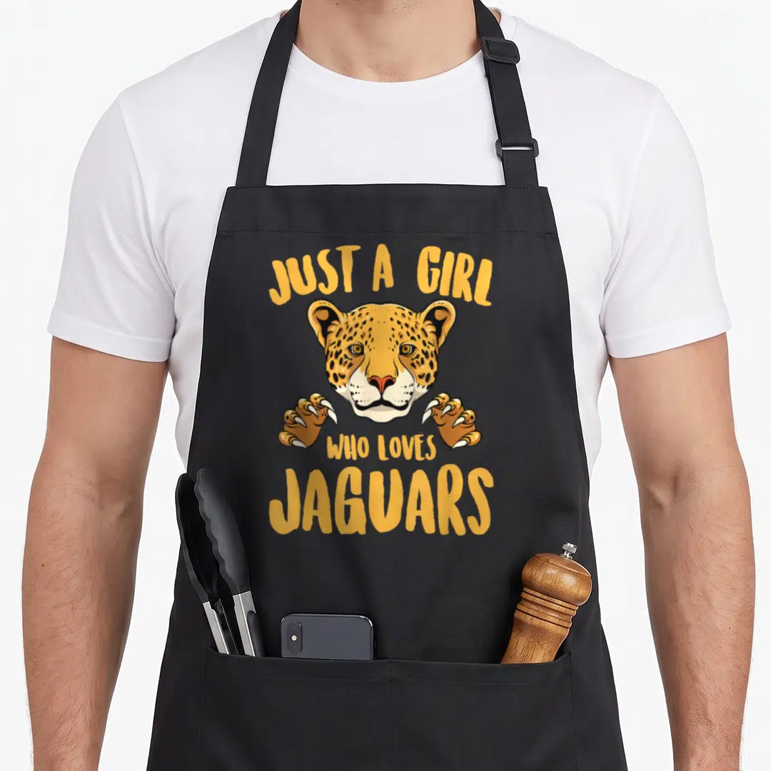 Cute animal apron for grilling - Cartoon jaguar head and paws between yellow text reading Just A Girl Who Loves Jaguars — shown on a black cotton canvas apron against a white background