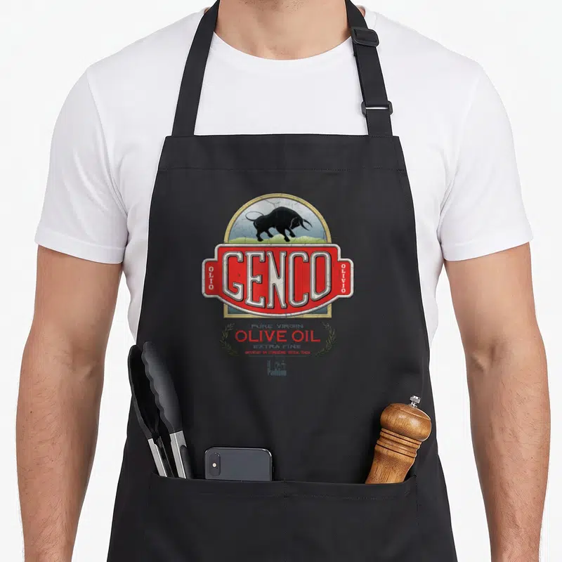 Godfather oil apron - Genco olive oil label with black bull, red rectangle, and olive branches in retro style — shown on a black cotton canvas apron against a white background