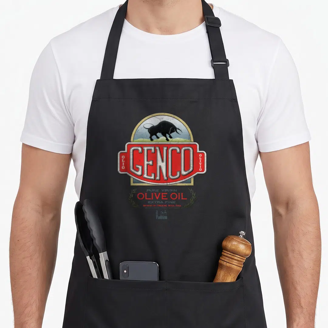 Godfather oil apron - Genco olive oil label with black bull, red rectangle, and olive branches in retro style — shown on a black cotton canvas apron against a white background